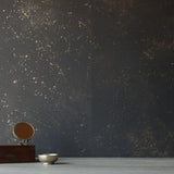 A table with knick knacks stands in front of a wall papered in a random splattered pattern in metallic gold on a black field.