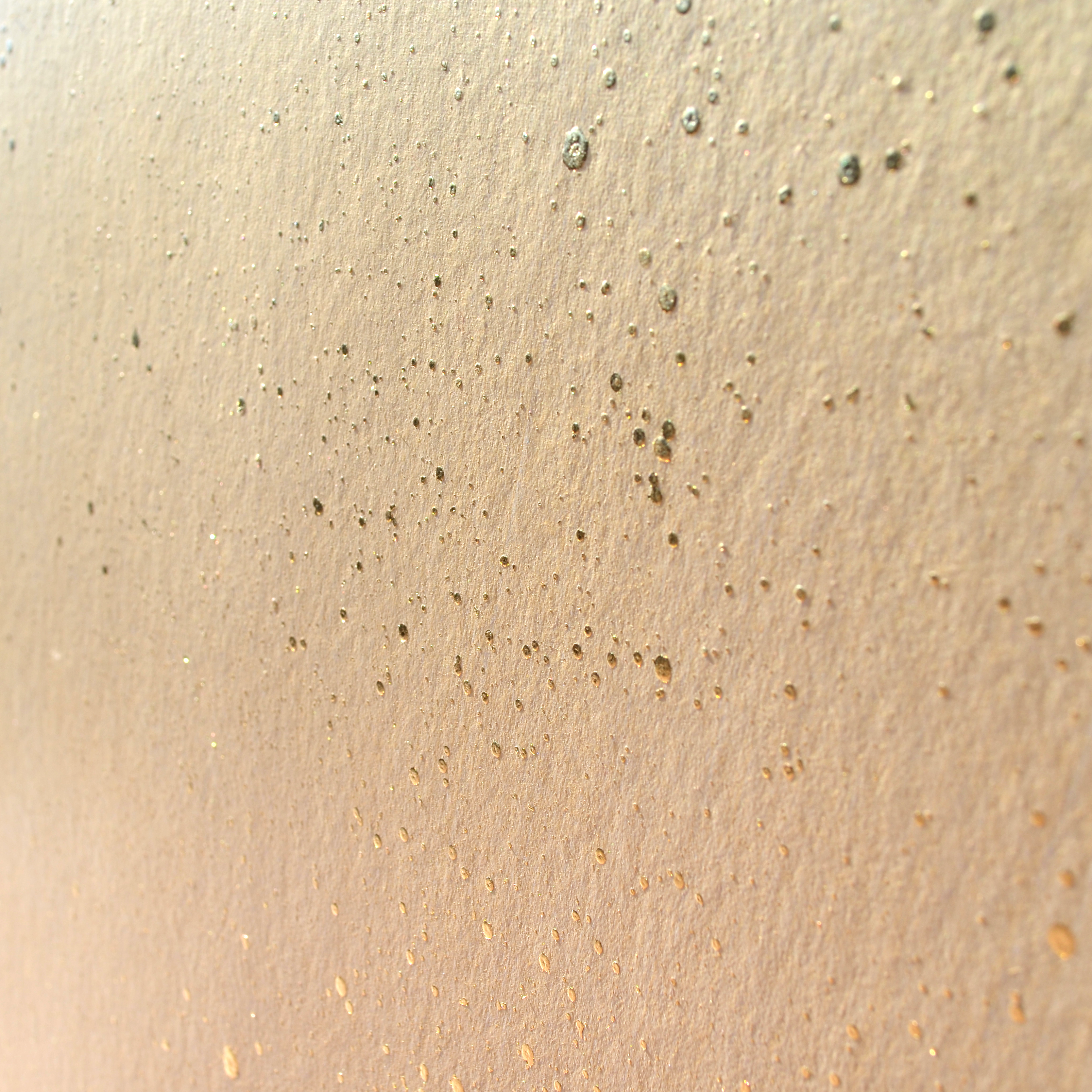Wide-angle shot of wallpaper in a random splattered pattern in metallic gold on a cream field.