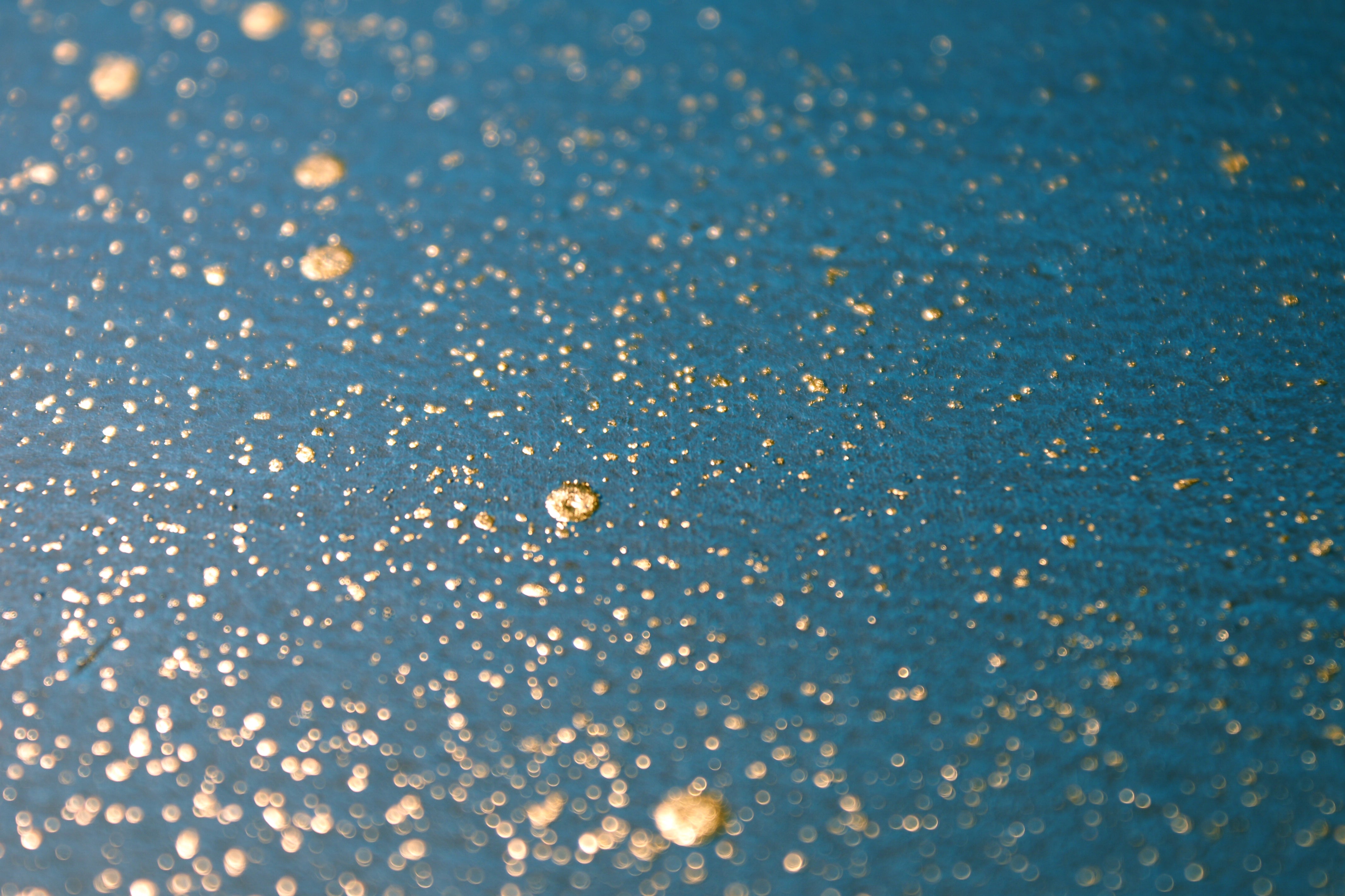 Wide-angle shot of wallpaper in a random splattered pattern in metallic gold on a blue field.