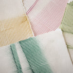 Pile of wallpaper swatches with dimensional combed patterns in green, gold and pink colorways on cream fields.