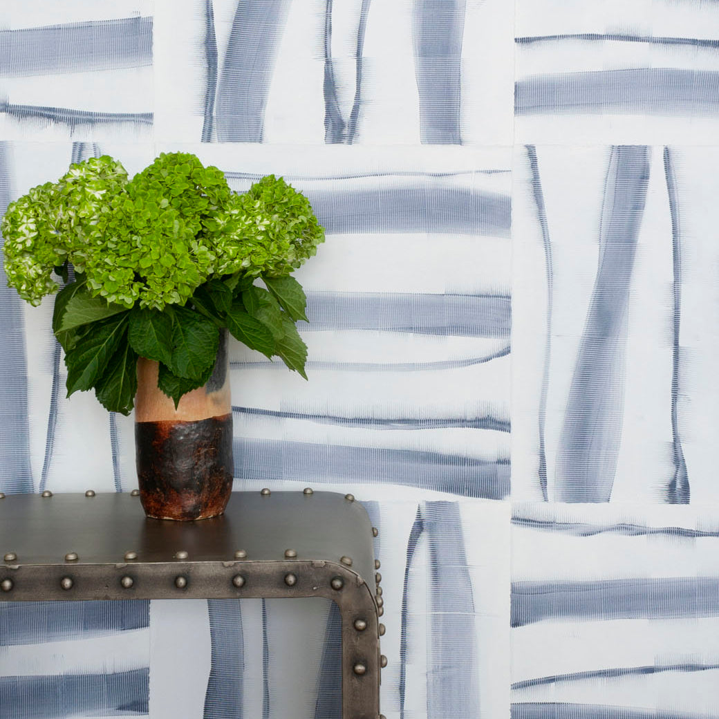 Flowers on a metal end table in front of a wall covered in an irregular combed stripe wallpaper in navy on a white field.