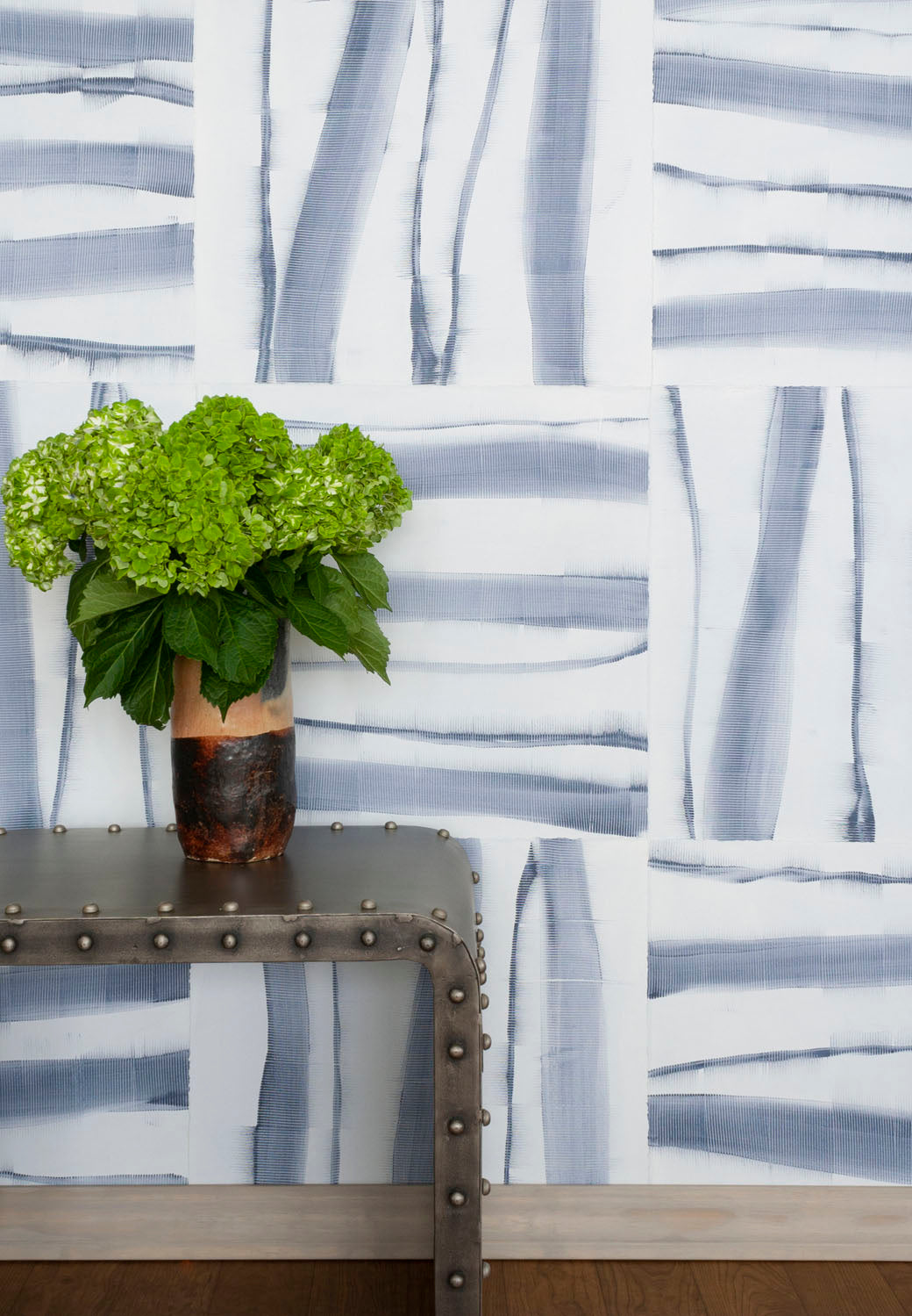 Flowers on a metal end table in front of a wall covered in an irregular combed stripe wallpaper in navy on a white field.