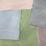 Pile of wallpaper swatches with irregular brushed patterns in shades of blue, green, gray and pink.