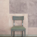 A chair stands in front of a wall papered in a domino pattern in sheets of dusty rose and mauve.