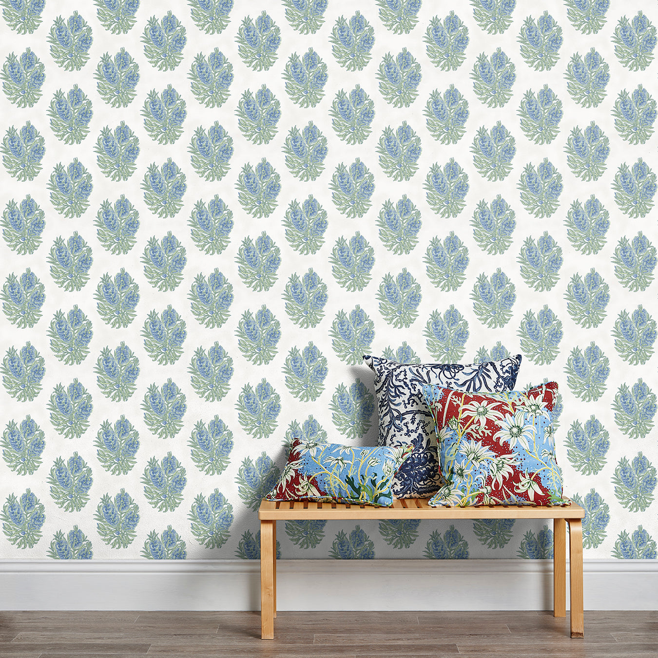 A stool stacked with throw pillows in front of a wall papered in a floral cameo print in light blue, green and white.