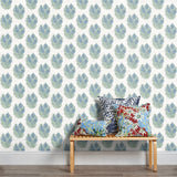 A stool stacked with throw pillows in front of a wall papered in a floral cameo print in light blue, green and white.