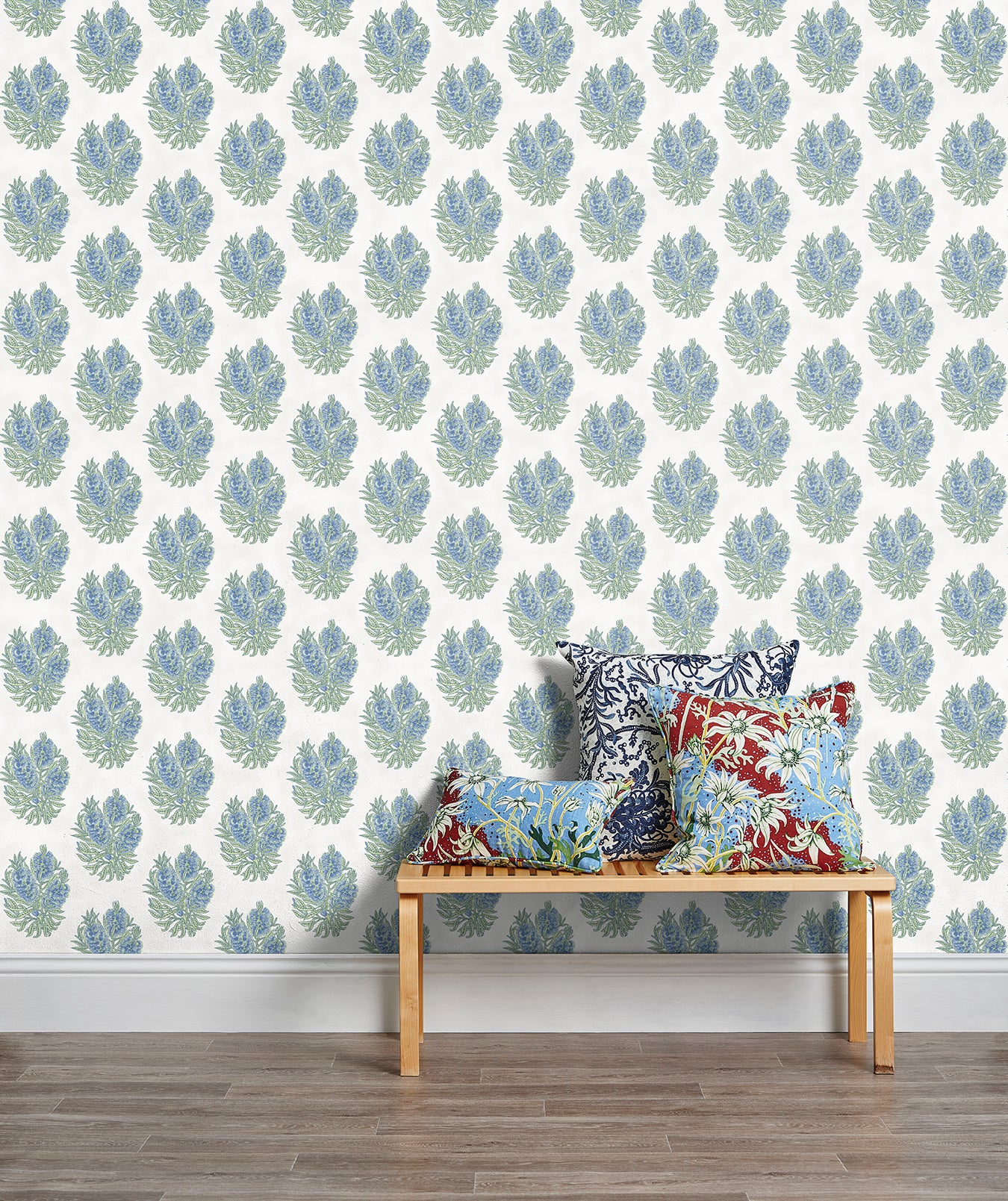 A stool stacked with throw pillows in front of a wall papered in a floral cameo print in light blue, green and white.