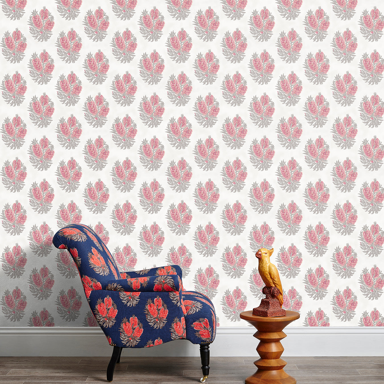 Armchair and end table in front of a wall papered in a floral cameo print in dusty rose, gray and white.