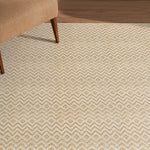 Beige patterned rug on a wooden floor with a partial view of a brown chair.