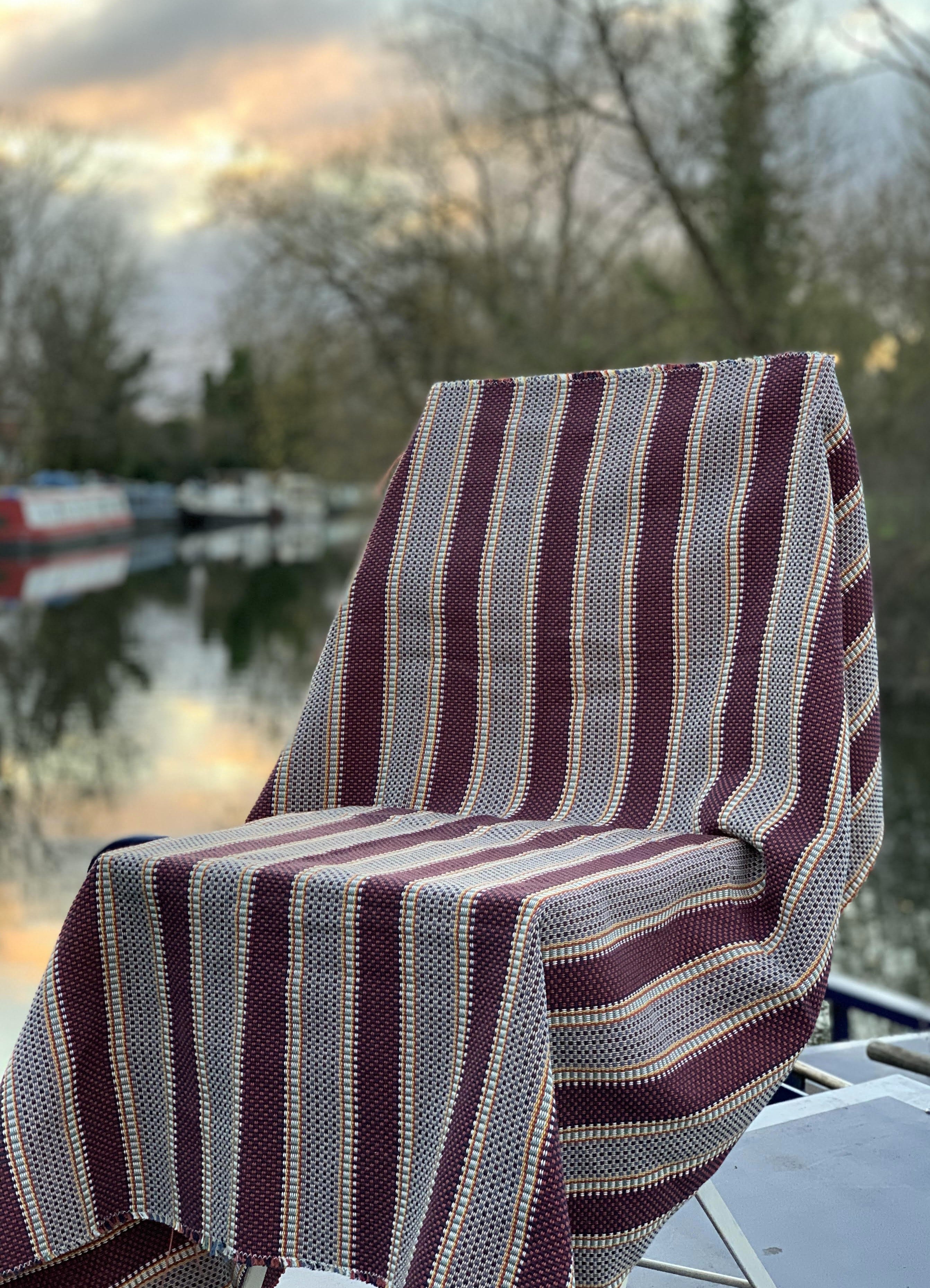 Striped fabric draped over a chair with a blurred background of water and trees
