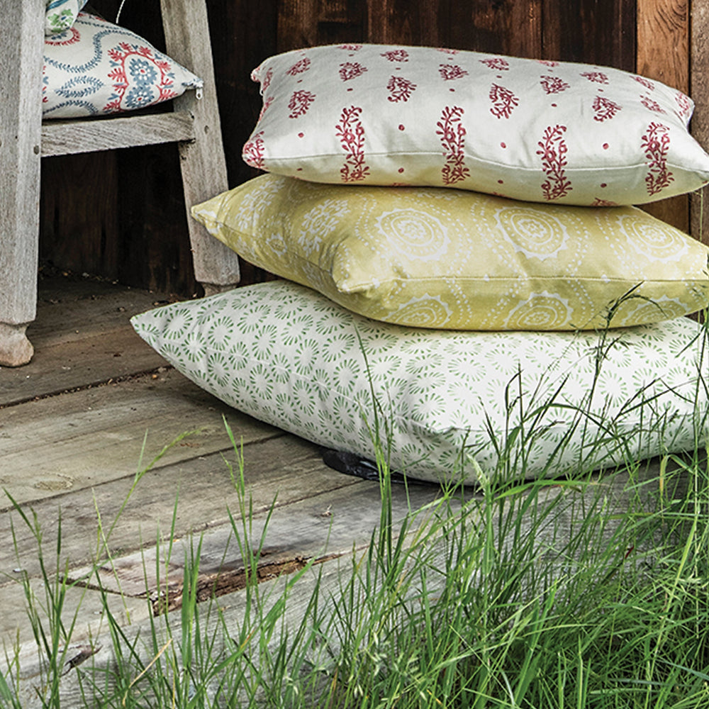 An outdoors shot of a pile of throw pillows in a variety of different patterns in shades of red, white, green and yellow.