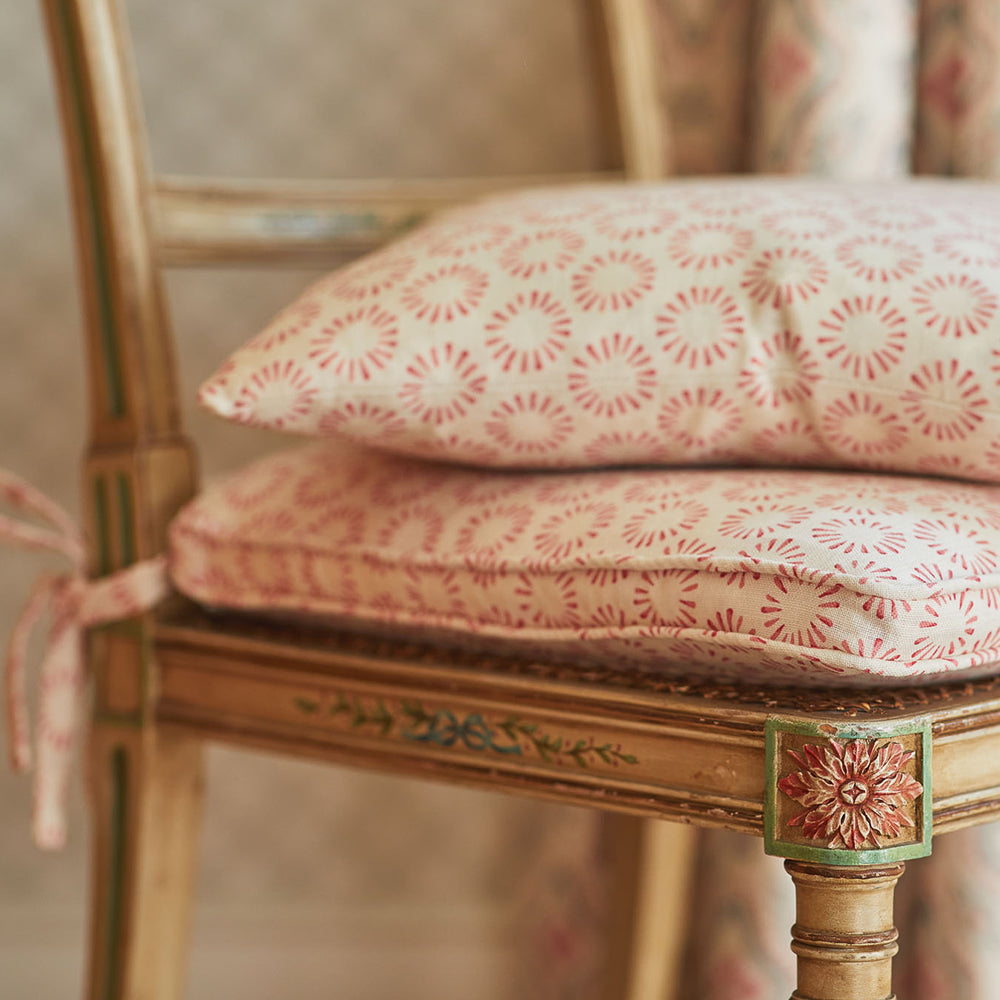 Close-up of a wooden chair topped with a cushion and throw pillow, both in the same playful circular print in red and cream. 