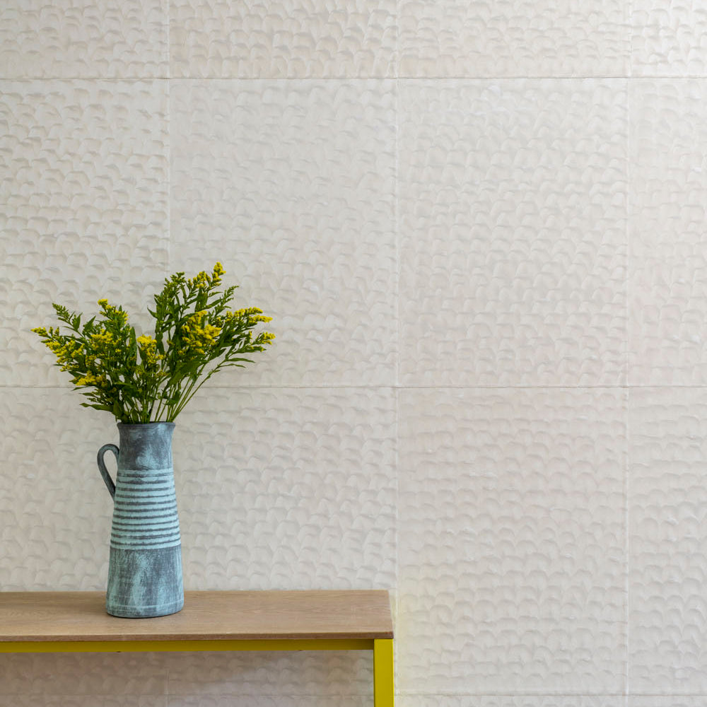 An end table with a vase of flowers stand in front of a wall papered in a repeating dappled texture in cream.