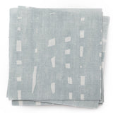 A stack of fabric swatches in a painterly small-scale grid print in blue-gray on a white field.