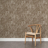 A wooden chair stands in front of a wall papered in a painterly small-scale grid print in brown on a white field.