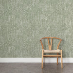 A wooden chair stands in front of a wall papered in a painterly small-scale grid print in sage on a white field.