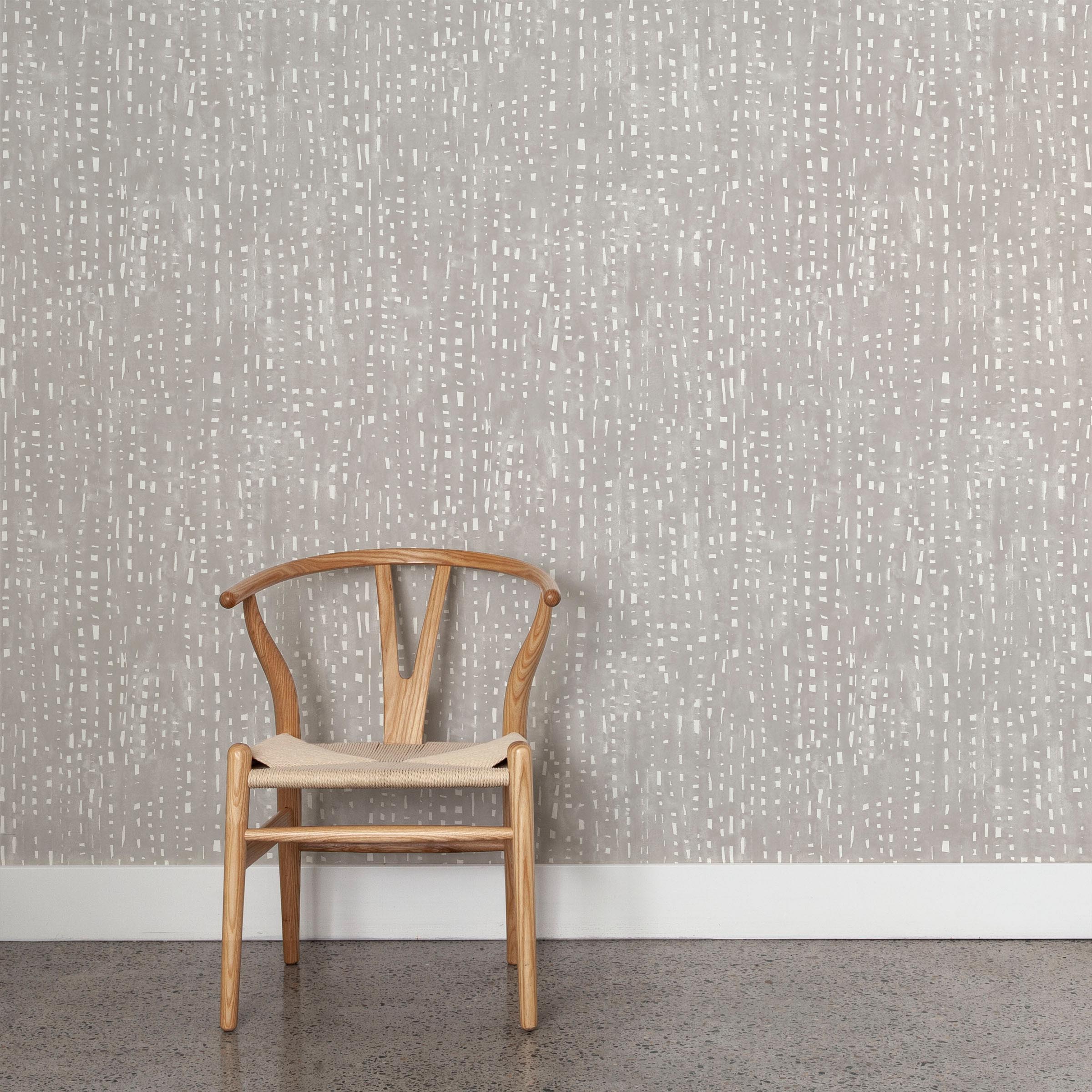 A wooden chair stands in front of a wall papered in a painterly small-scale grid print in gray on a white field.