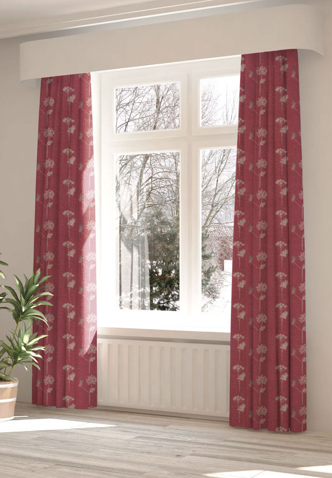 A large, sunny window with long curtains in a flower and butterfly print on a red field.