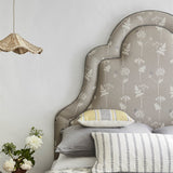 A bed covered in throw pillows and with an upholstered headboard covered in a flower and butterfly print.