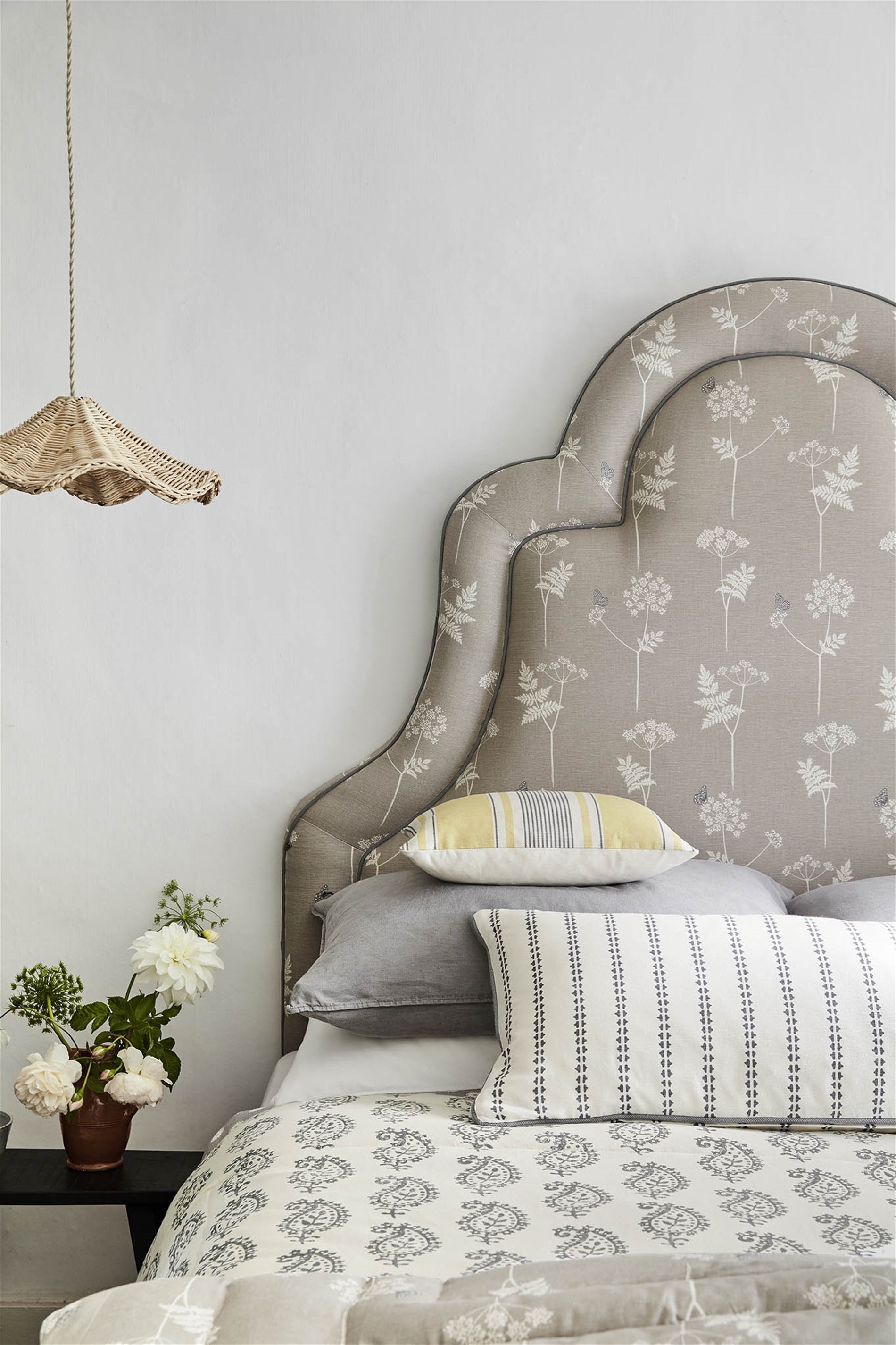 A bed covered in throw pillows and with an upholstered headboard covered in a flower and butterfly print.