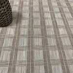 Close-up of a checkered patterned carpet with a rattan stool in the corner.