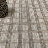 Close-up of a checkered patterned carpet with a rattan stool in the corner.