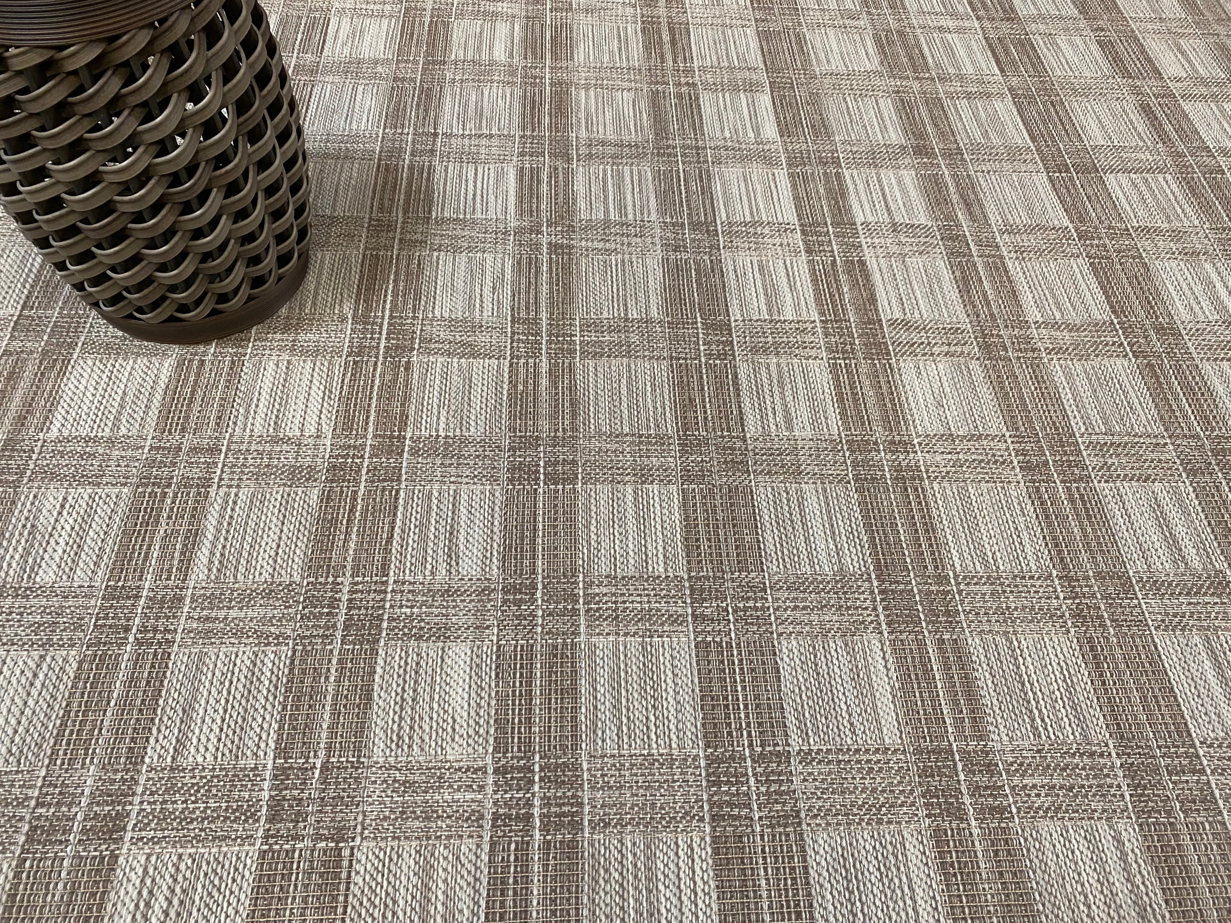 Close-up of a checkered patterned carpet with a rattan stool in the corner.
