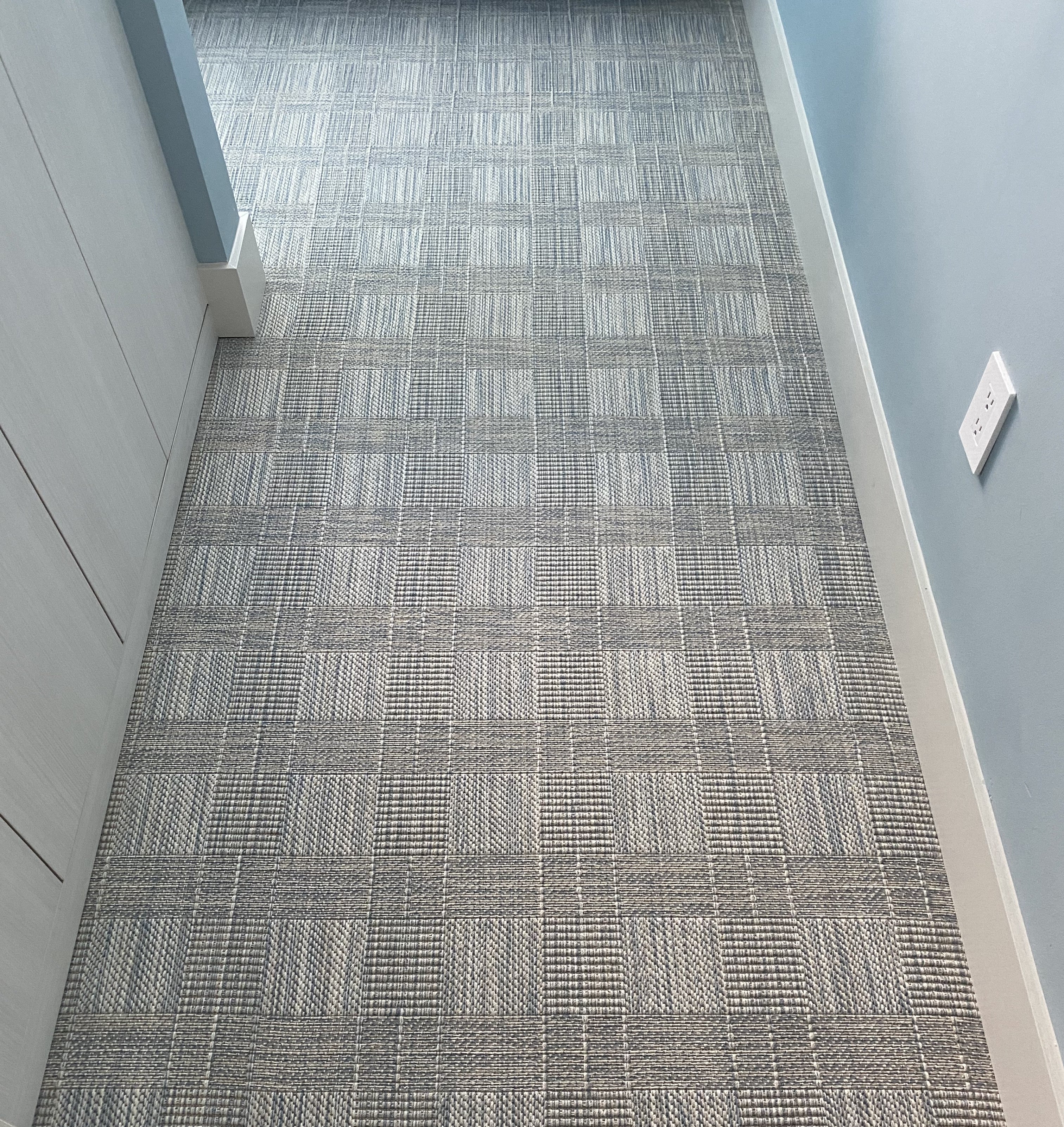 Patterned check blue carpet in a hallway with light blue walls.