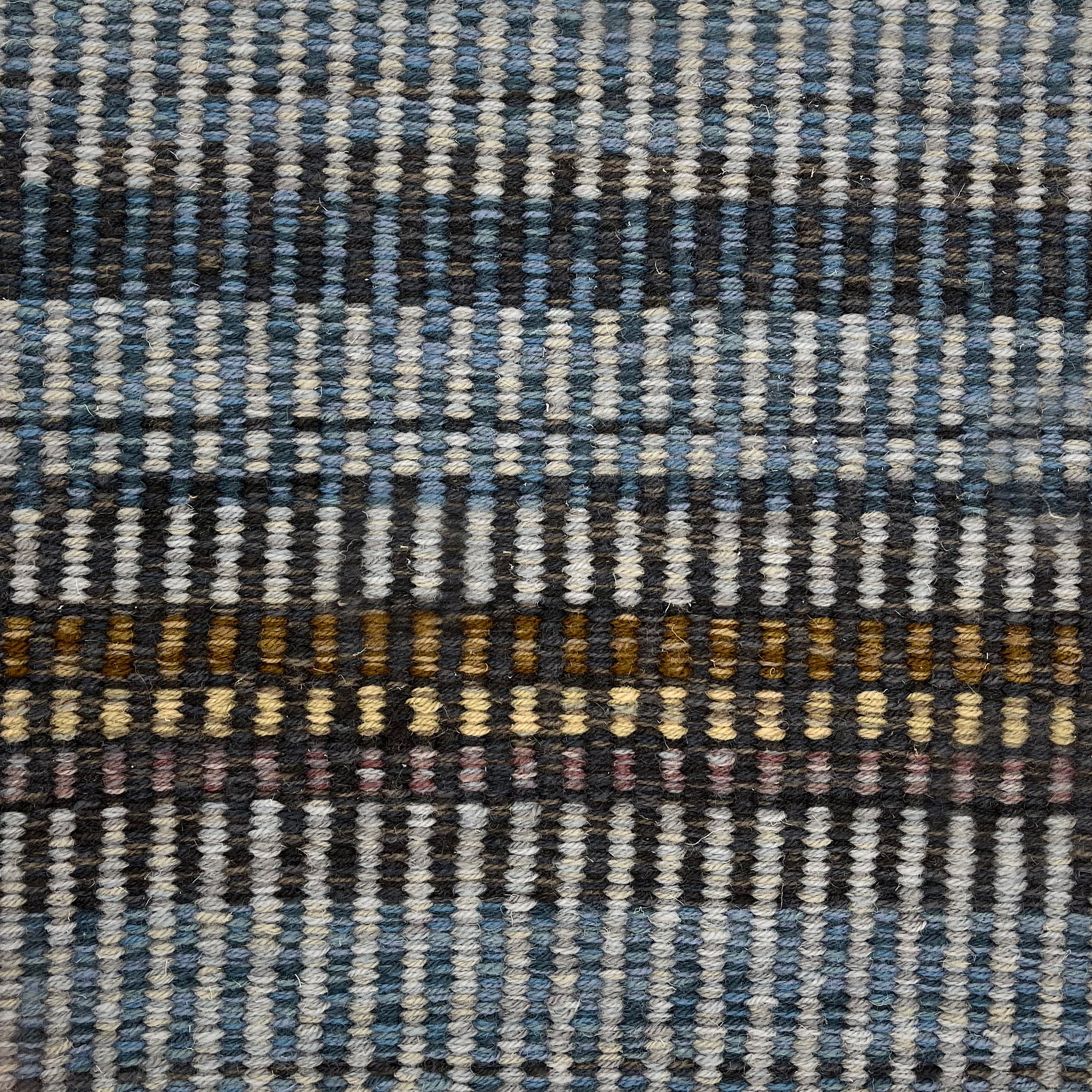 Handwoven carpet in a variegated stripe in shades of blue blue, charcoal, brown,  yellow and tan. 