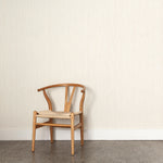 A wooden chair stands in front of a wall papered in a painterly stripe pattern in cream on a white field.