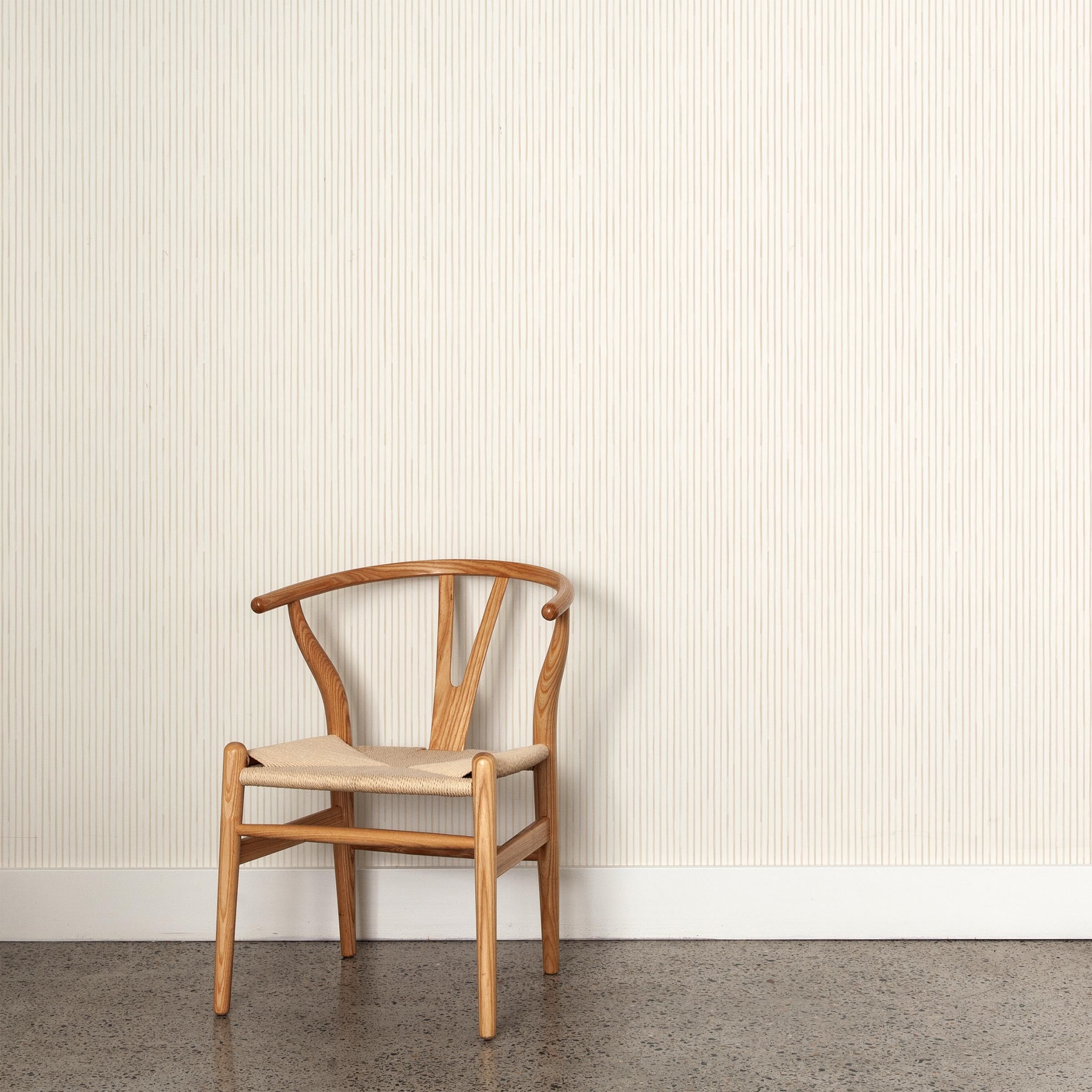 A wooden chair stands in front of a wall papered in a painterly stripe pattern in cream on a white field.