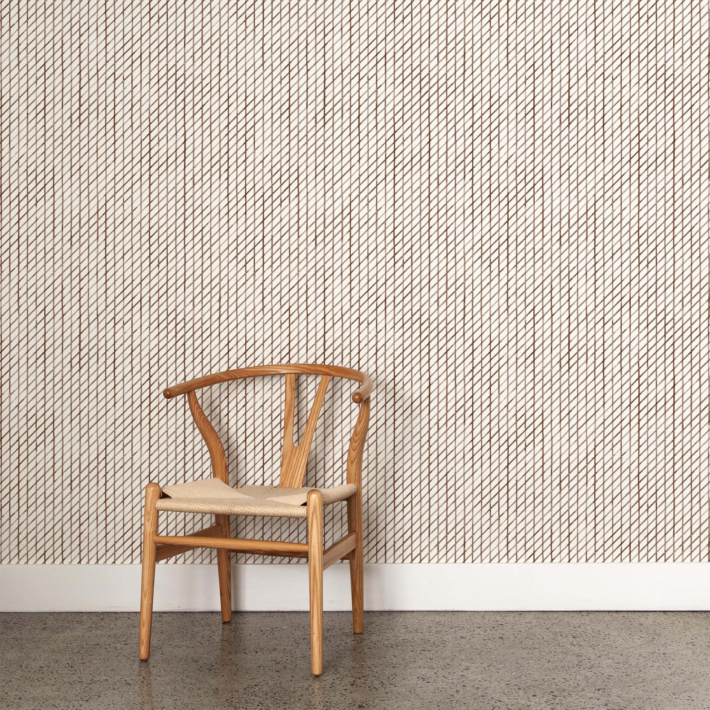 A wooden chair stands in front of a wall papered in a painterly uneven grid pattern in brown on a white field.