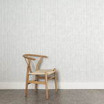 A wooden chair stands in front of a wall papered in a painterly uneven grid pattern in light blue on a white field.