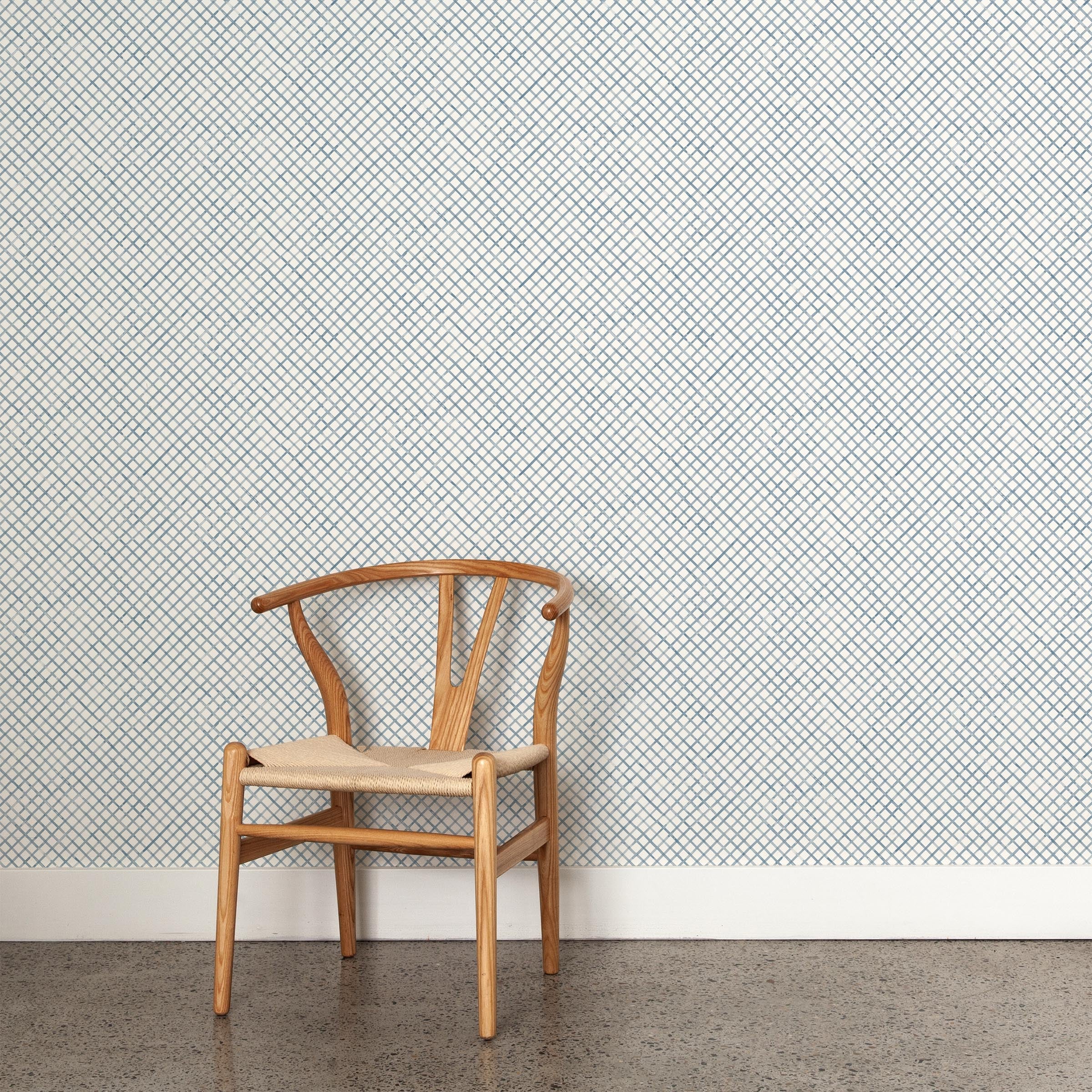 A wooden chair stands in front of a wall papered in a painterly grid pattern in navy on a white field.