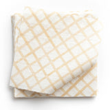 A stack of fabric swatches in a painterly grid pattern in gold on a white field.