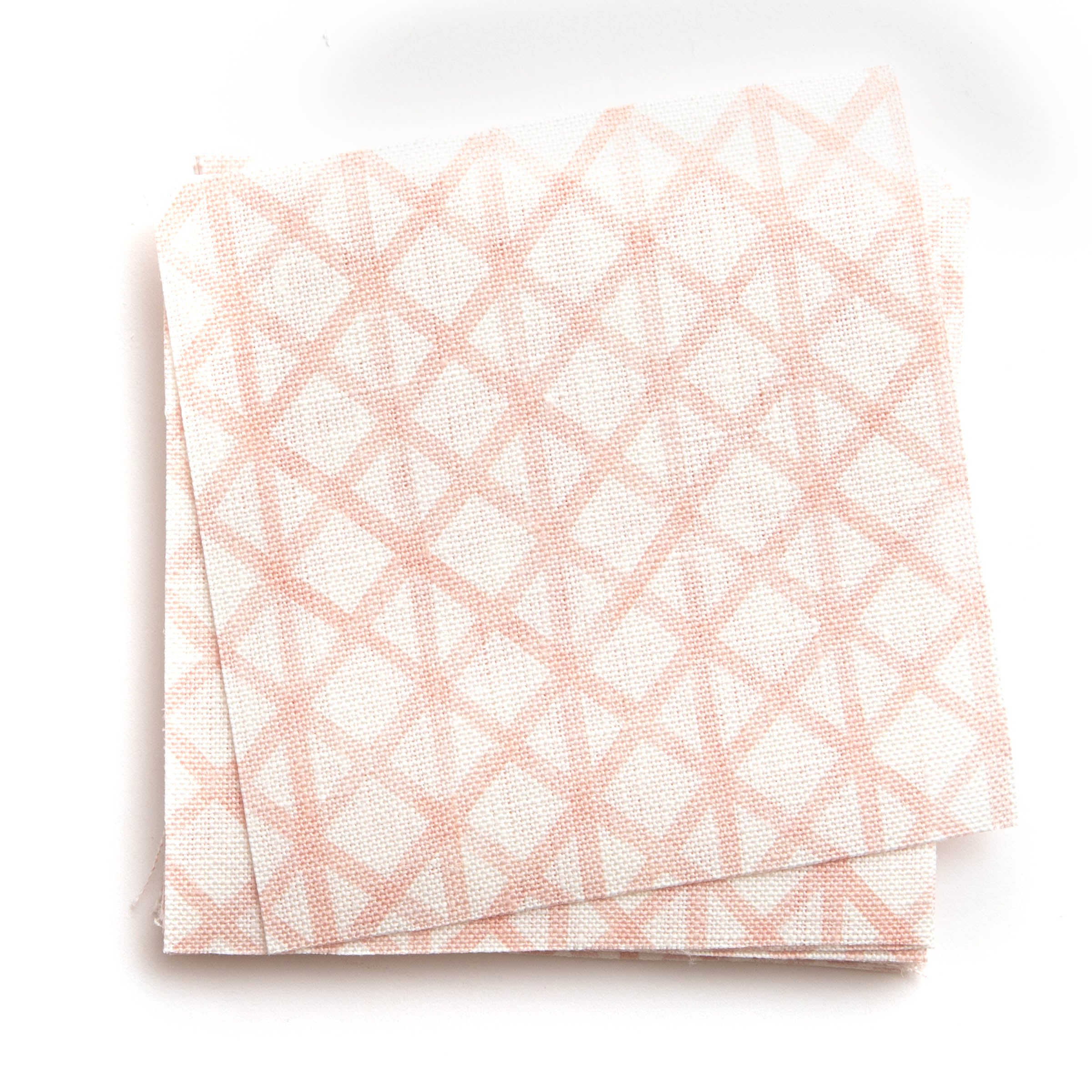 A stack of fabric swatches in an intricate striped grid pattern in light pink on a white field.