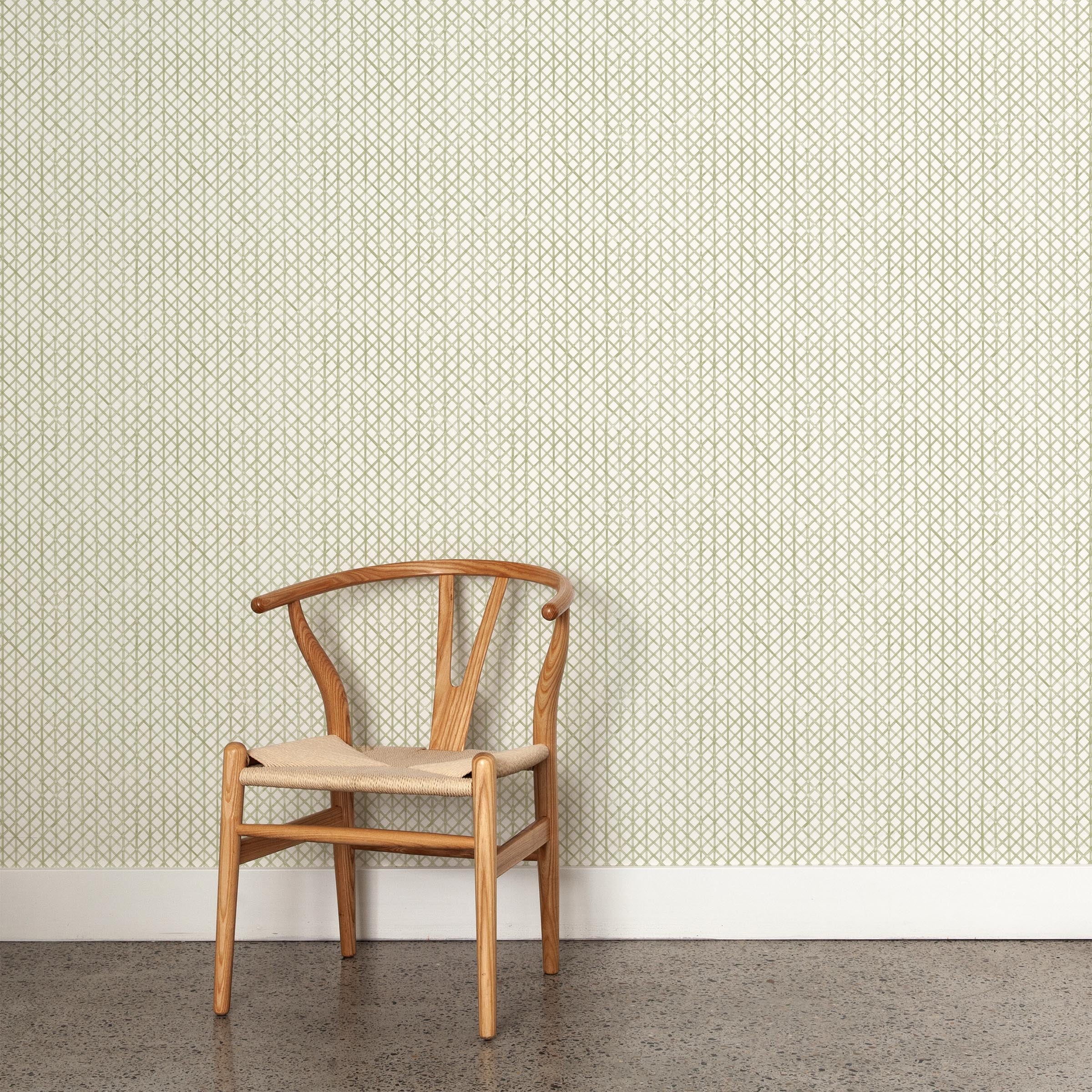 A wooden chair stands in front of a wall papered in an intricate striped grid pattern in sage on a white field.