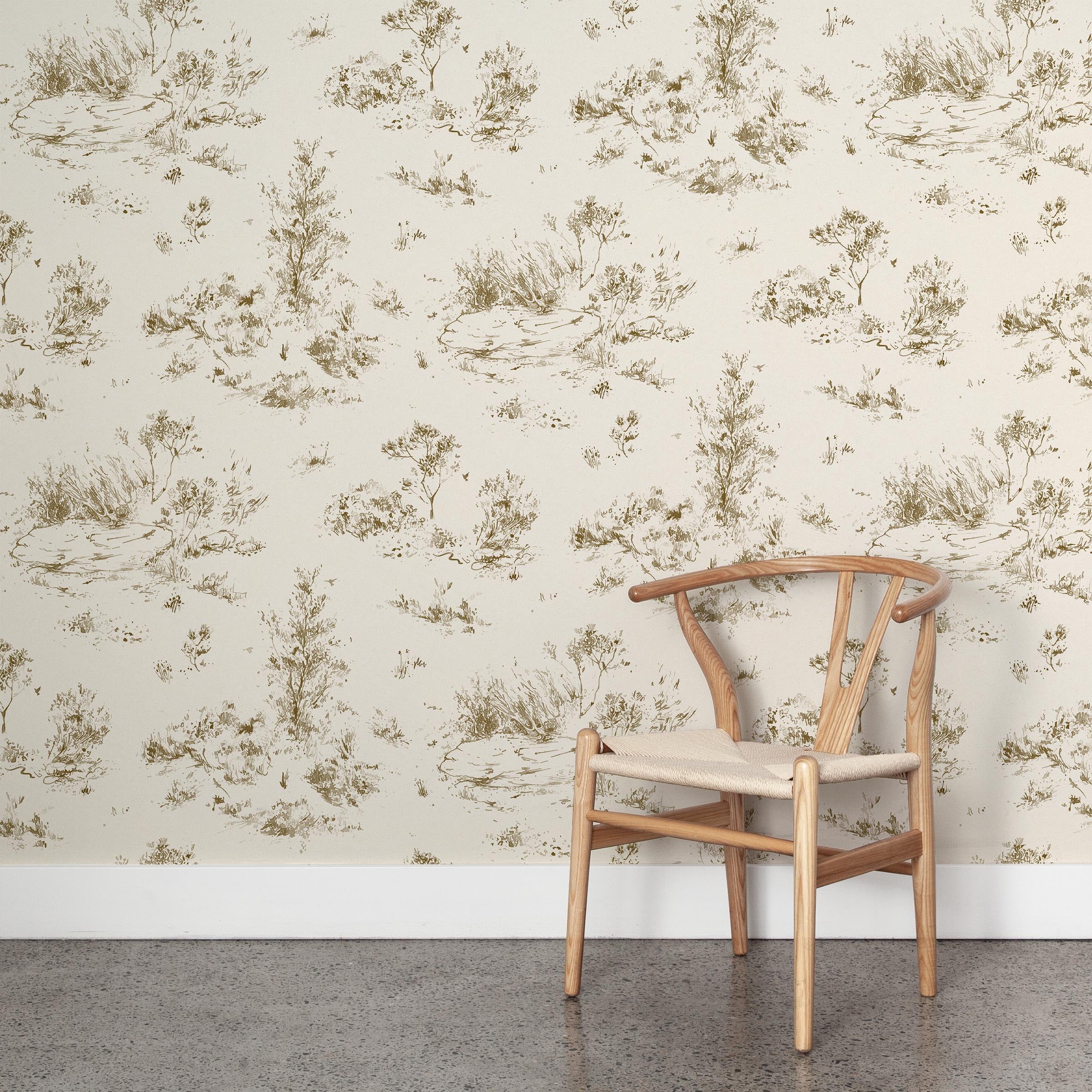 A wooden chair stands in front of a wall papered in a painterly shrub and tree print in bronze on a cream field.