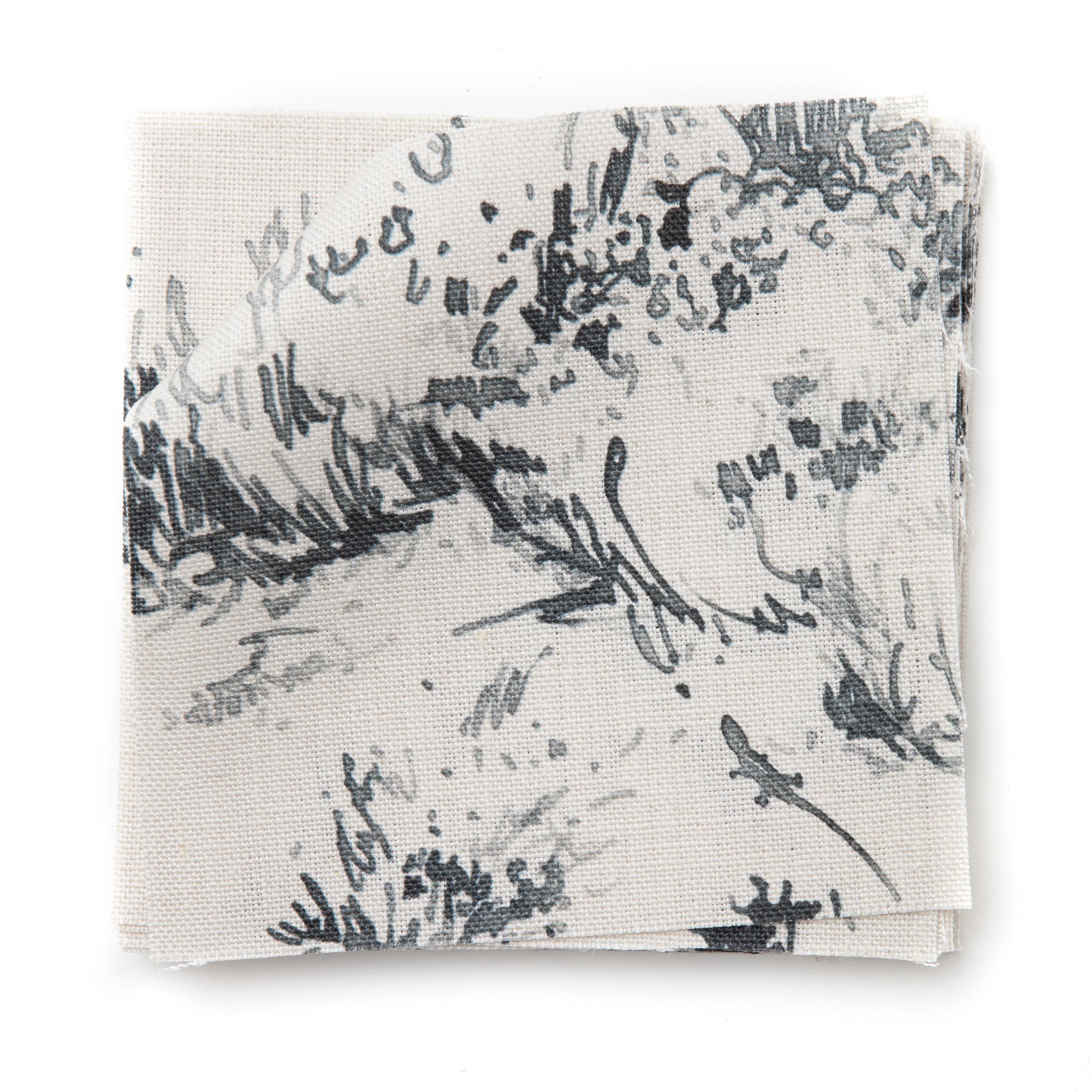 A stack of fabric swatches in a painterly shrub and tree print in navy on a cream field.