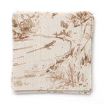 A stack of fabric swatches in a painterly shrub and tree print in bronze on a cream field.