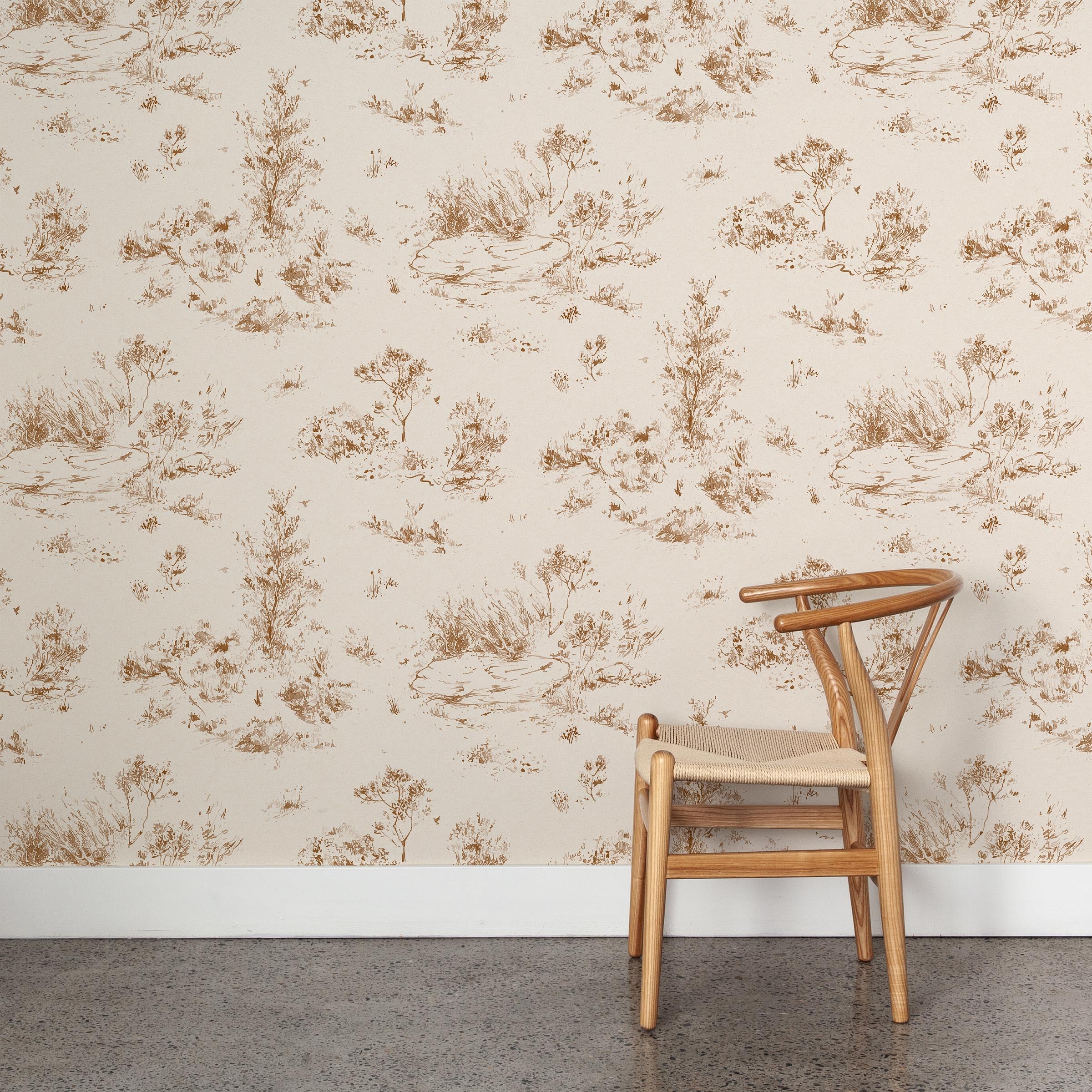 A wooden chair stands in front of a wall papered in a painterly shrub and tree print in sienna on a cream field.