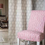 Close-up of a living room with a hanging curtain in a floral lattice print in white and cream on a tan field.