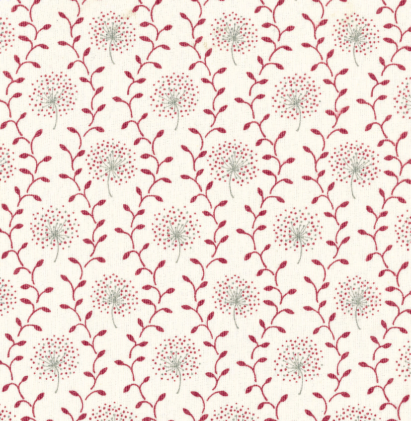 Detail of fabric in a repeating dandelion and leaf print in pink and red on a cream field.