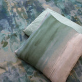 Throw pillows lay on top of fabric yardage in an abstract paint splotch print in shades of blue, green and tan.