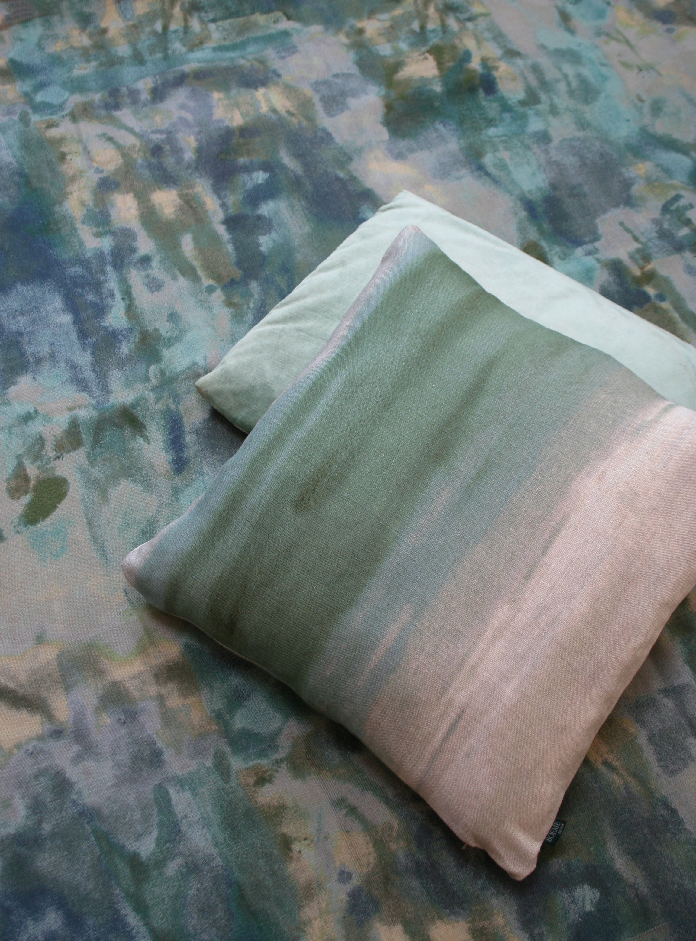 Throw pillows lay on top of fabric yardage in an abstract paint splotch print in shades of blue, green and tan.