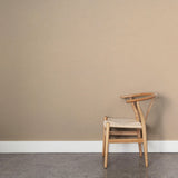 A wooden chair stands in front of a wall papered in a dotted diamond grid in white on a tan field.