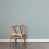 A wooden chair stands in front of a wall papered in a dotted diamond grid in white on a light blue field.