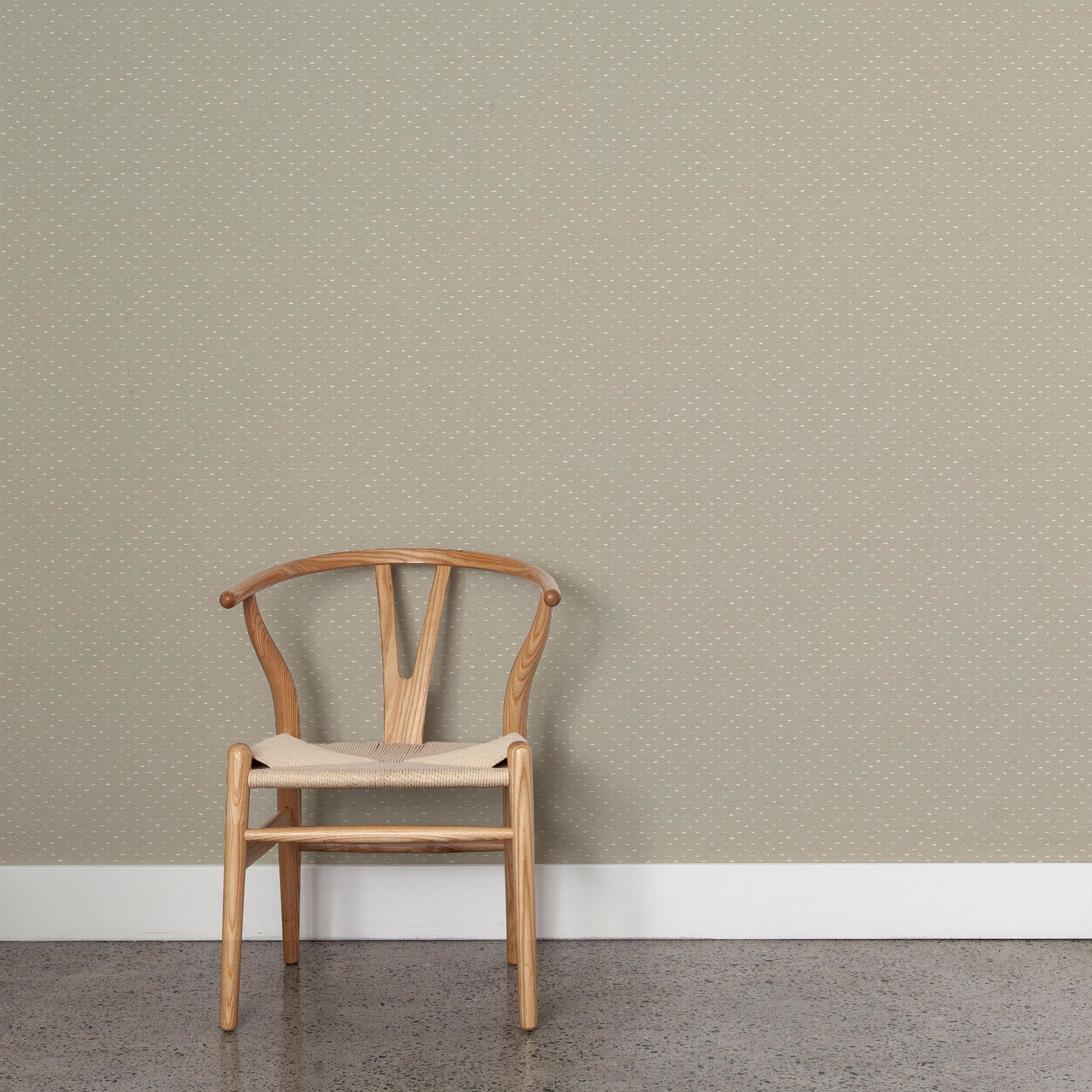 A wooden chair stands in front of a wall papered in a dotted diamond grid in white on a sage field.