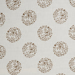 Detail of a printed cotton fabric in a repeating dotted pattern in brown on a cream field.