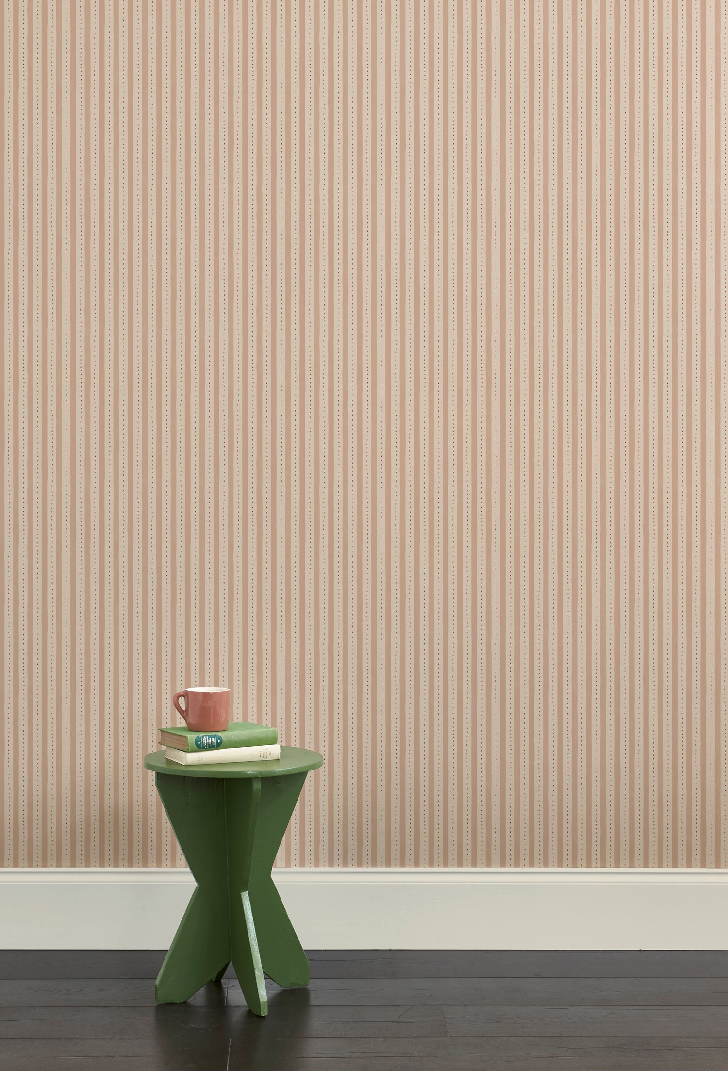 A green wooden stool with books and a mug against a Wallpaper playful hand drawn dotted stripe in blush.